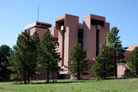 Exterior view of the NCAR Mesa Lab with pine trees, green grass, and blue sky. and 